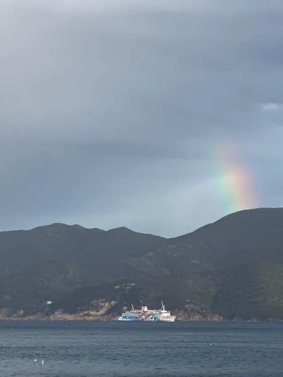 Un arcobaleno sopra le colline, con un traghetto in navigazione sul mare
