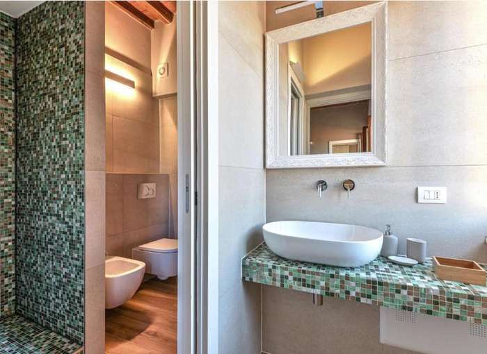 Bagno con mosaico verde, lavabo bianco, specchio con cornice e doccia