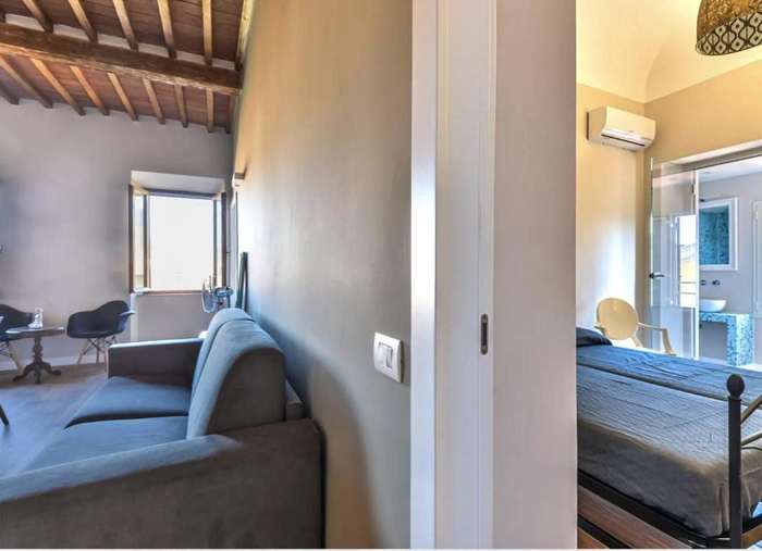 Divano grigio in soggiorno e, oltre la porta, una camera da letto