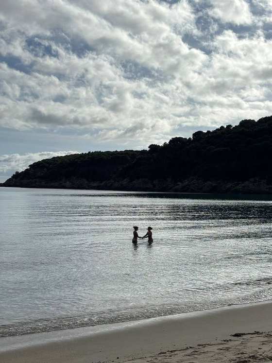 Due persone in controluce nell'acqua bassa, con la collina boscosa sullo sfondo
