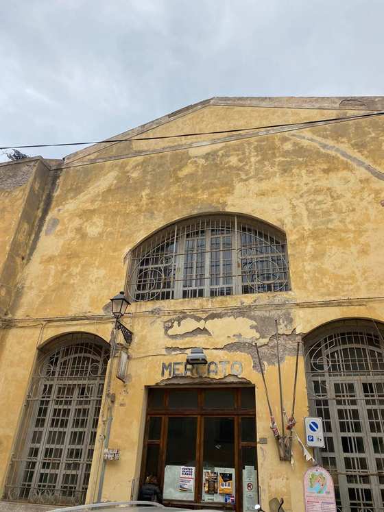 La facciata gialla e scrostata dell'edificio del mercato, con grandi finestre ad arco con inferriate