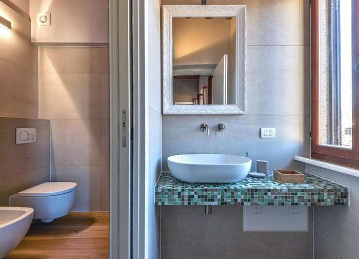 Lavabo bianco su piano in mosaico verde, con specchio e finestra