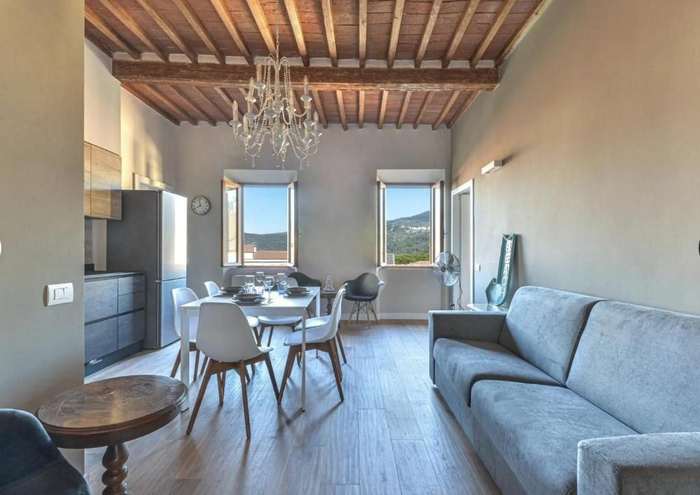 Soggiorno con travi a vista, tavolo da pranzo e divano, con due finestre sulle colline