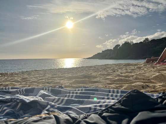 Il sole basso sul mare visto dalla sabbia, con un telo a righe in primo piano