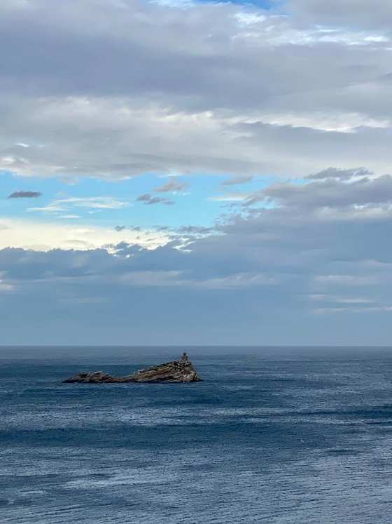 Uno scoglio con un piccolo faro in mezzo al mare, sotto un cielo di nuvole