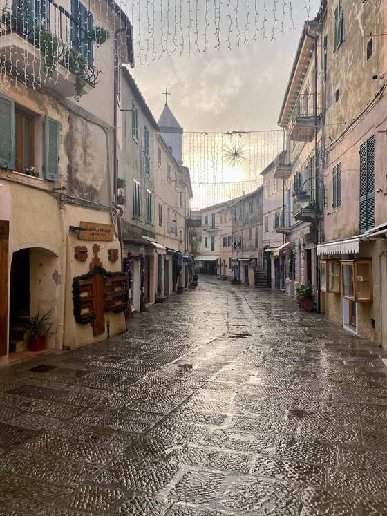 Una via del borgo con le luminarie, i campanili sullo sfondo e il selciato bagnato dalla pioggia